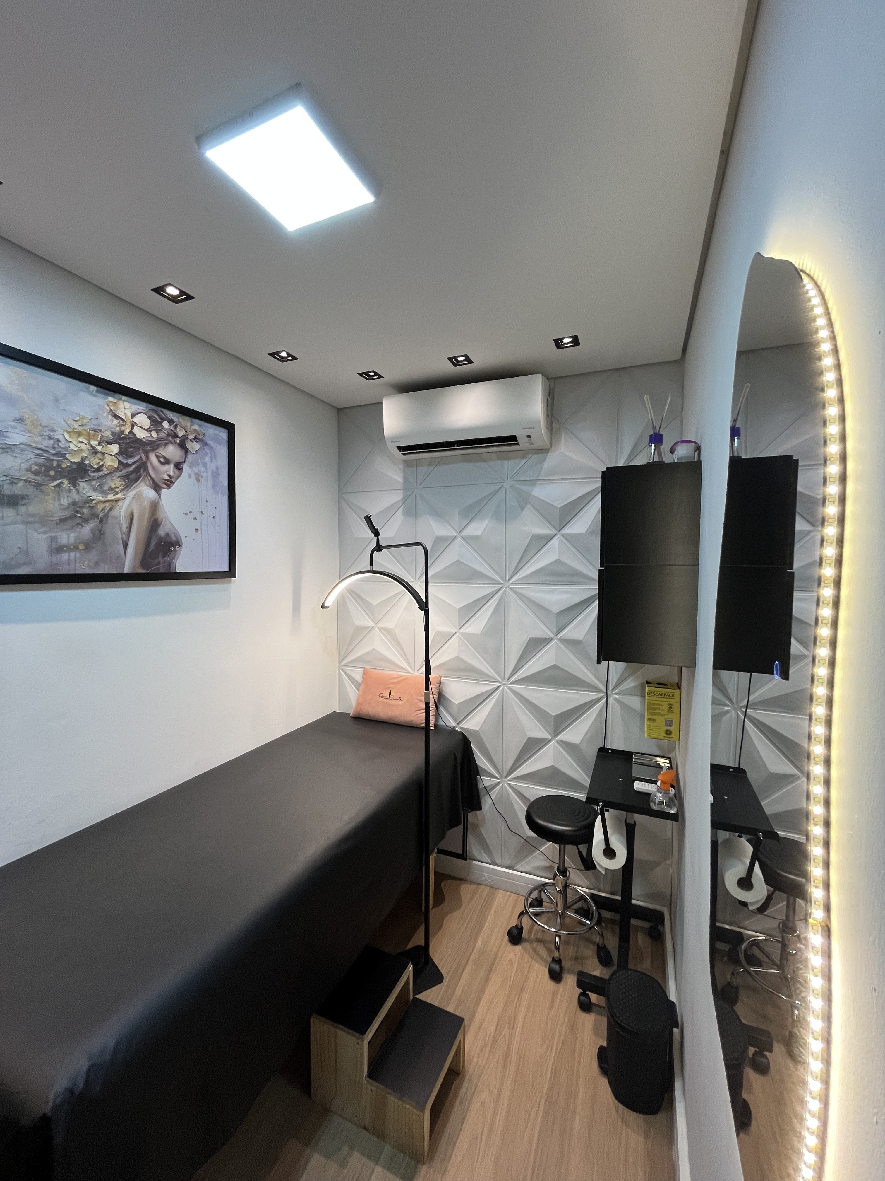 Sala de atendimento com maca preta, espelho com LED e ambiente clínico sofisticado